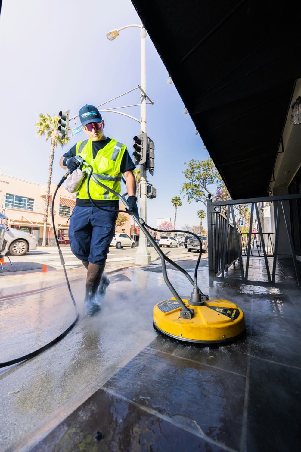 Pressure washing technician cleaning a storefront sidewalk with a surface cleaner